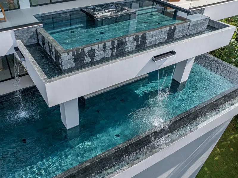 The glass-walled pool seen from below, cantilevered over the slope